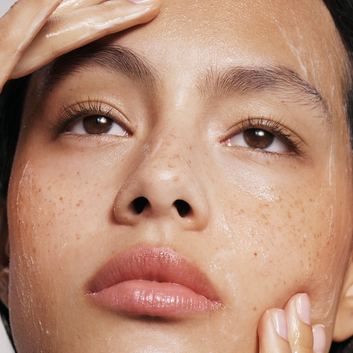 Model applying skincare on clean skin.