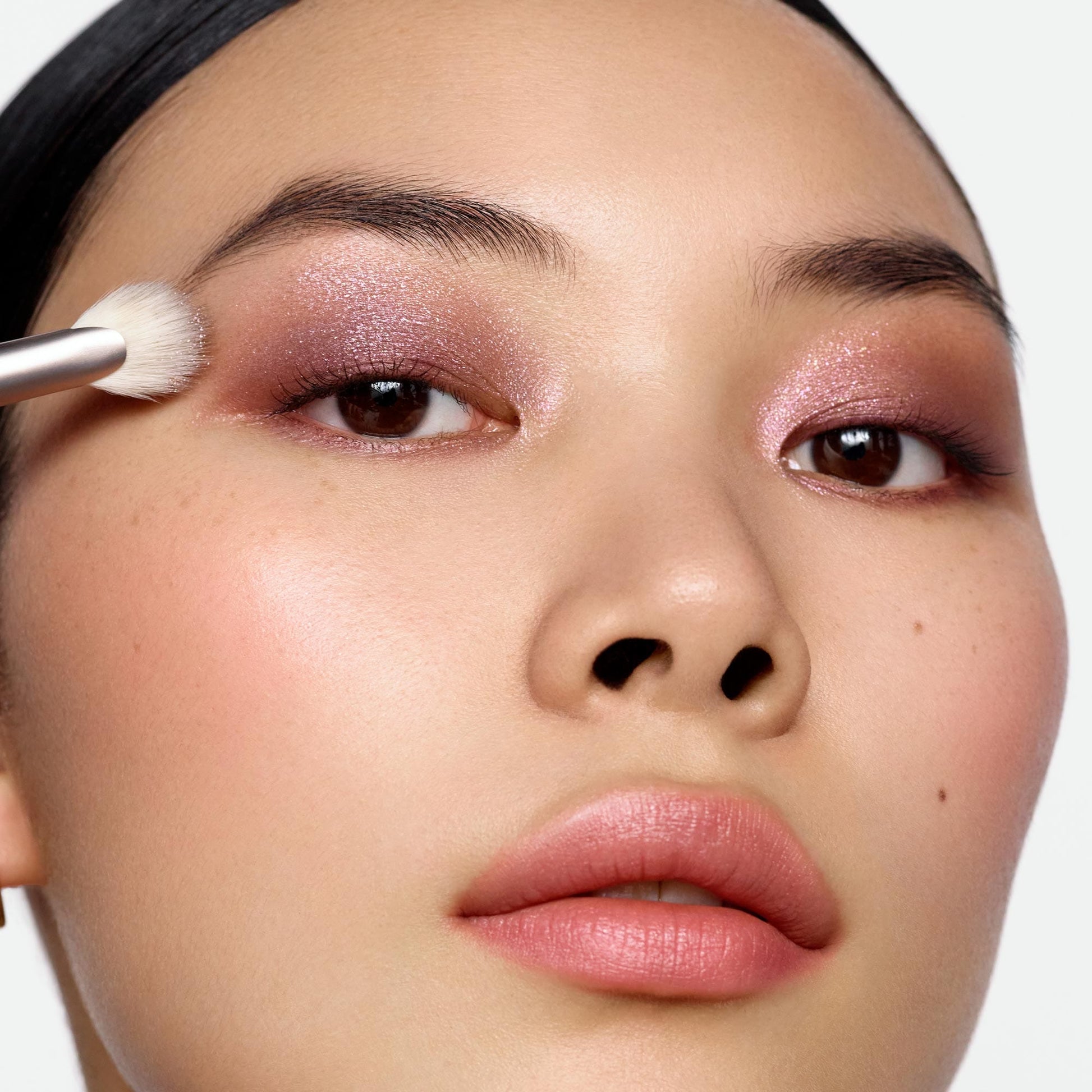 Model using Rose Inc Number 7 Eyeshadow Fan Brush to apply Shimmer eyeshadow to eyelid