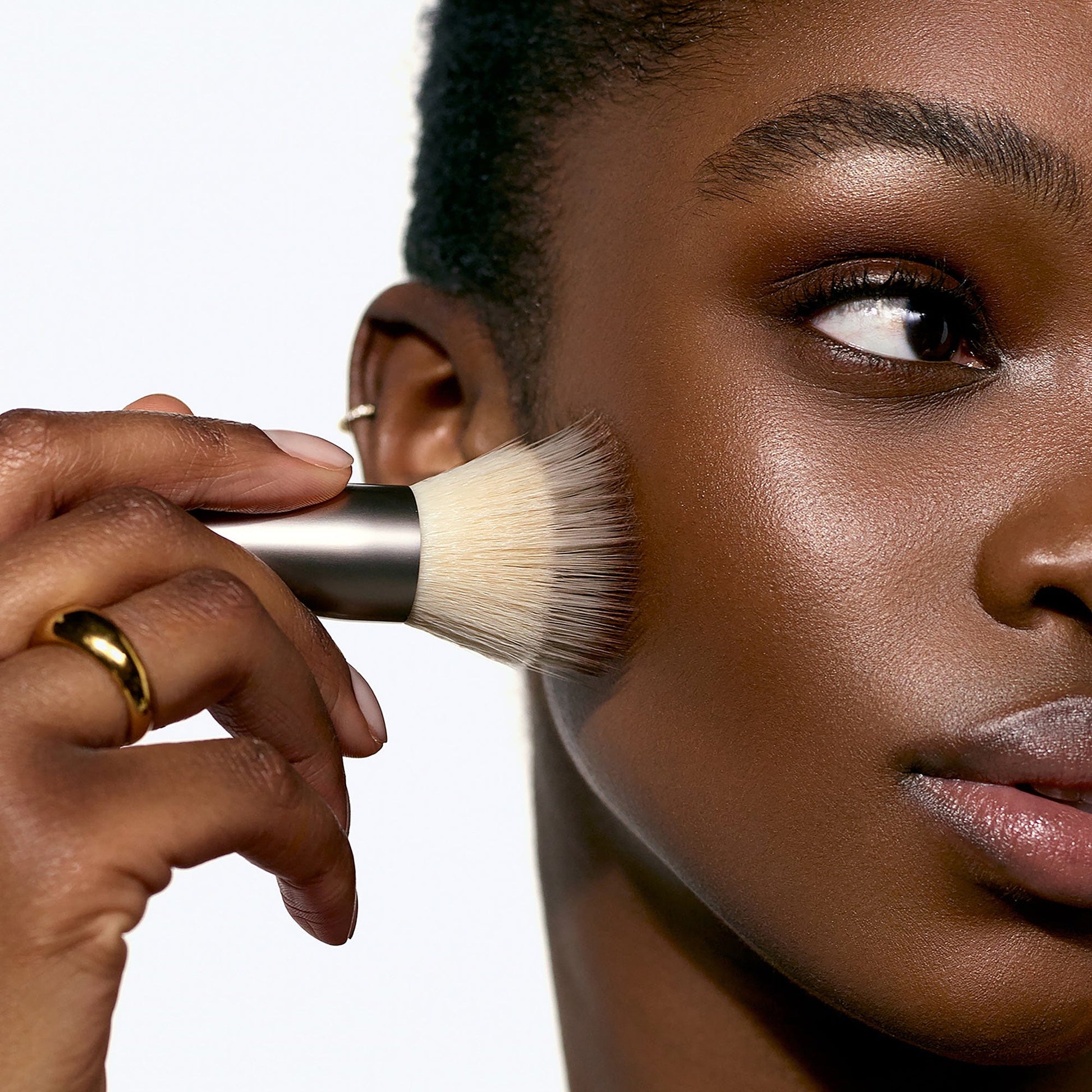 Model Awa applying the Solar Infusion Soft-Focus  Cream Bronzer in shade Capri on cheekbones with the Number 5 Bronzer brush.